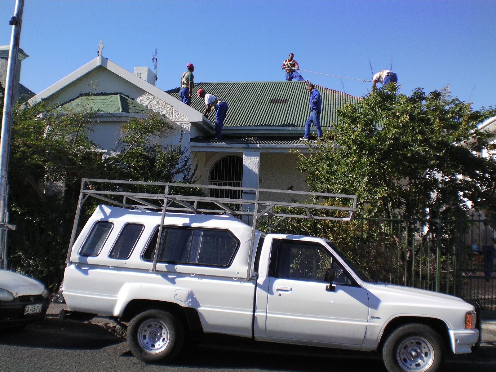 Roof replacement work with multiple workers in blue uniforms installing corrugated metal sheeting on residential house.