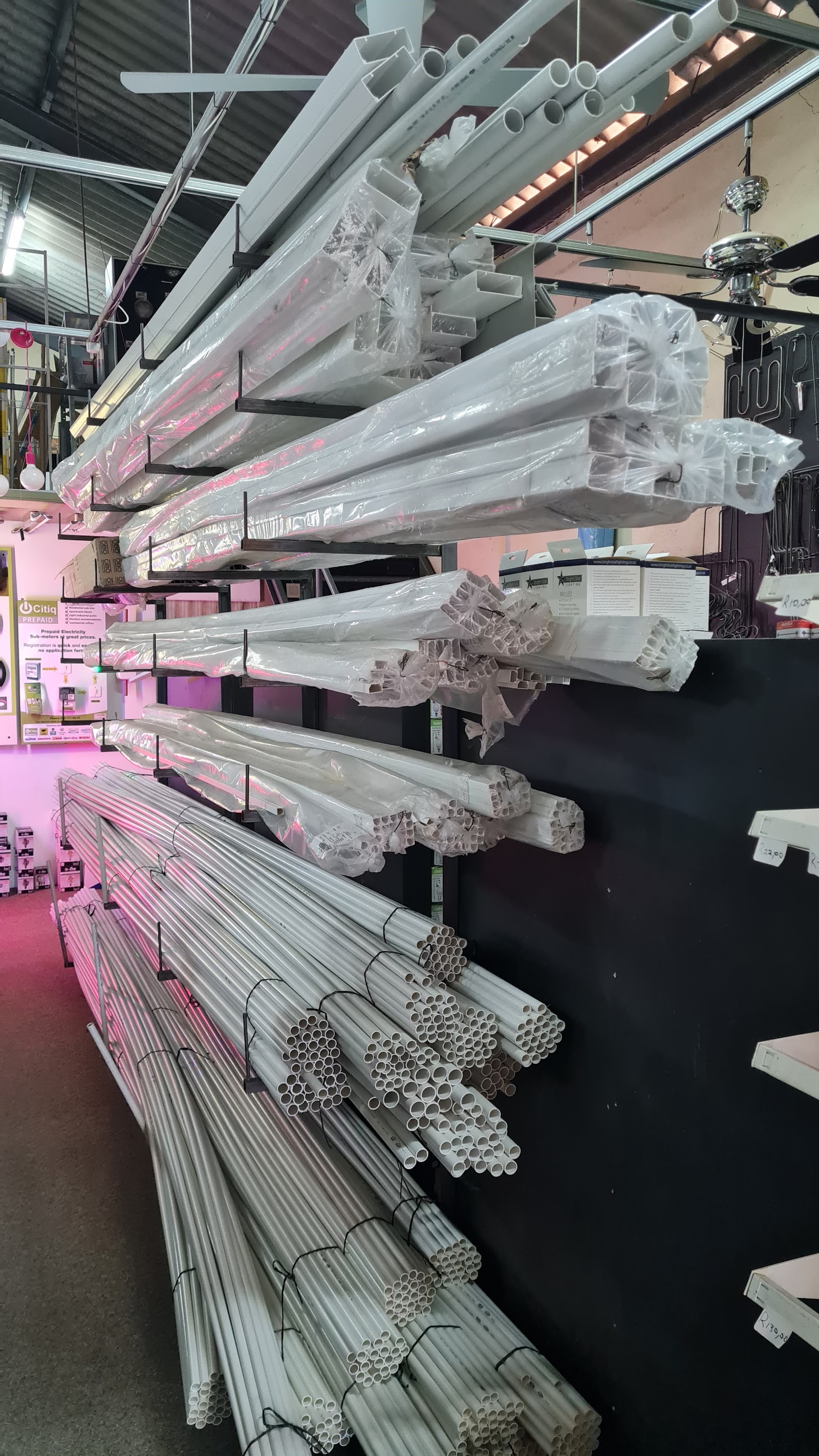 Warehouse shelving with bundled PVC pipes and electrical conduit tubing wrapped in plastic, organized by size.