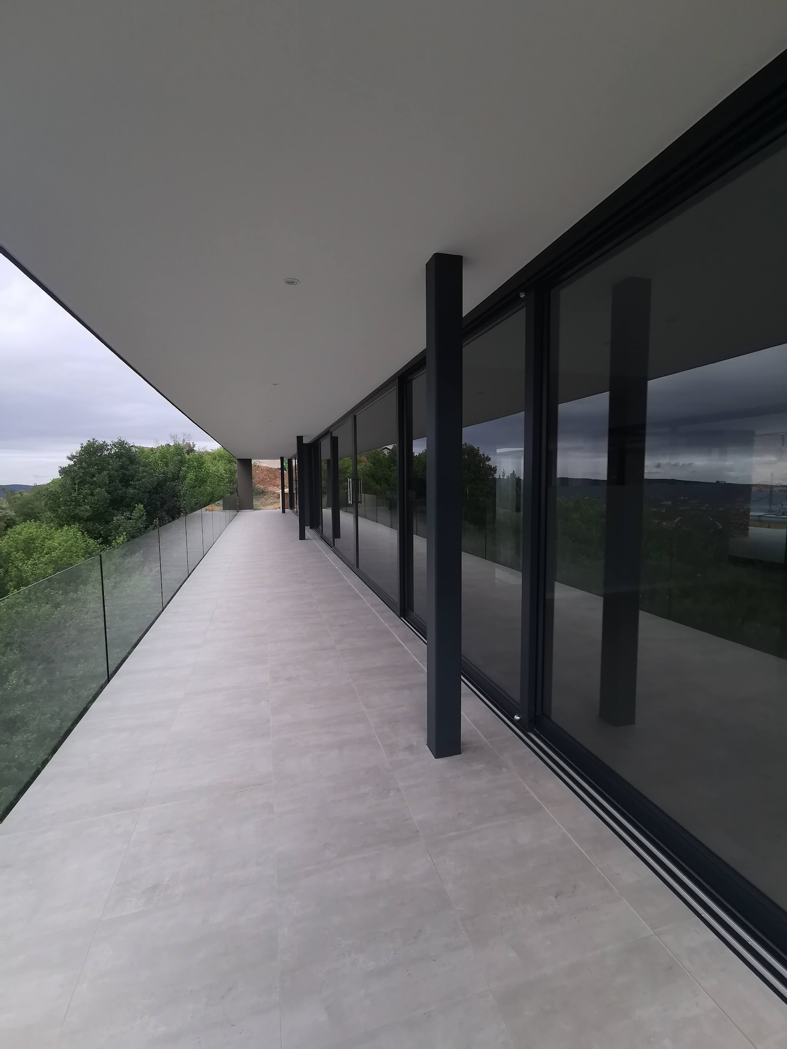 Modern building exterior terrace with black structural posts, glass railings, composite decking, and countryside views.