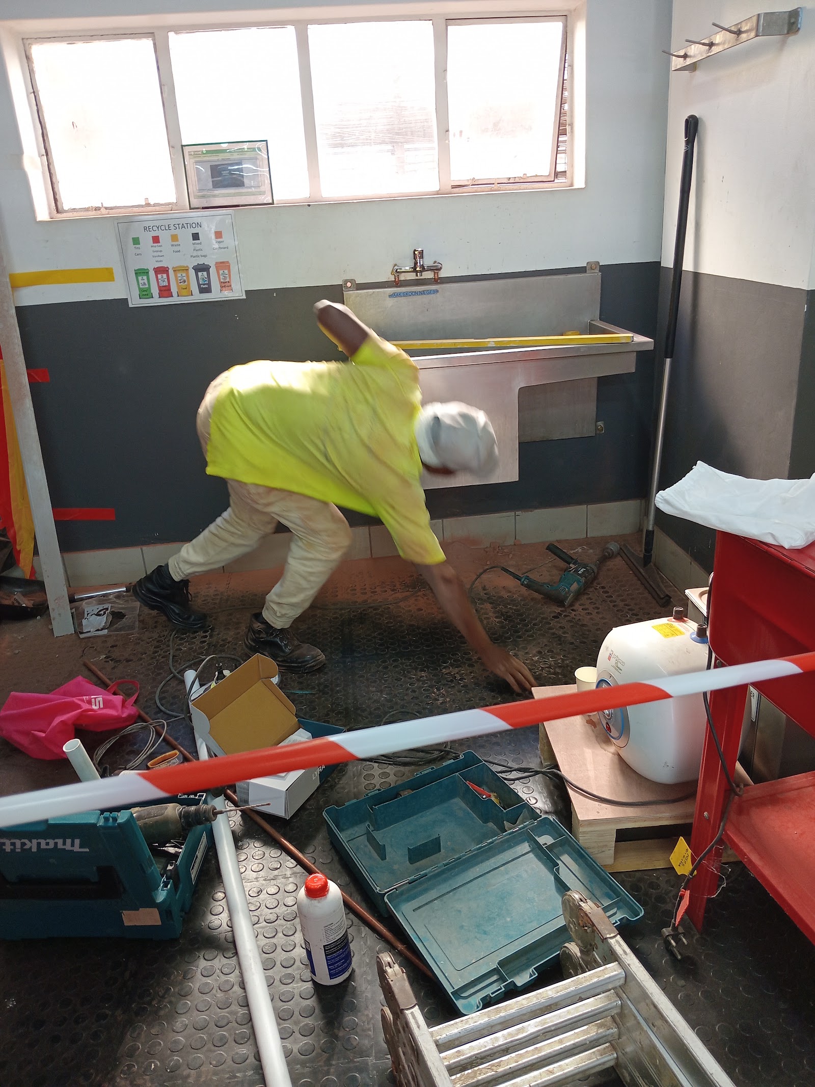 Worker in yellow safety vest installing bathroom fixtures with hand tools indoors.