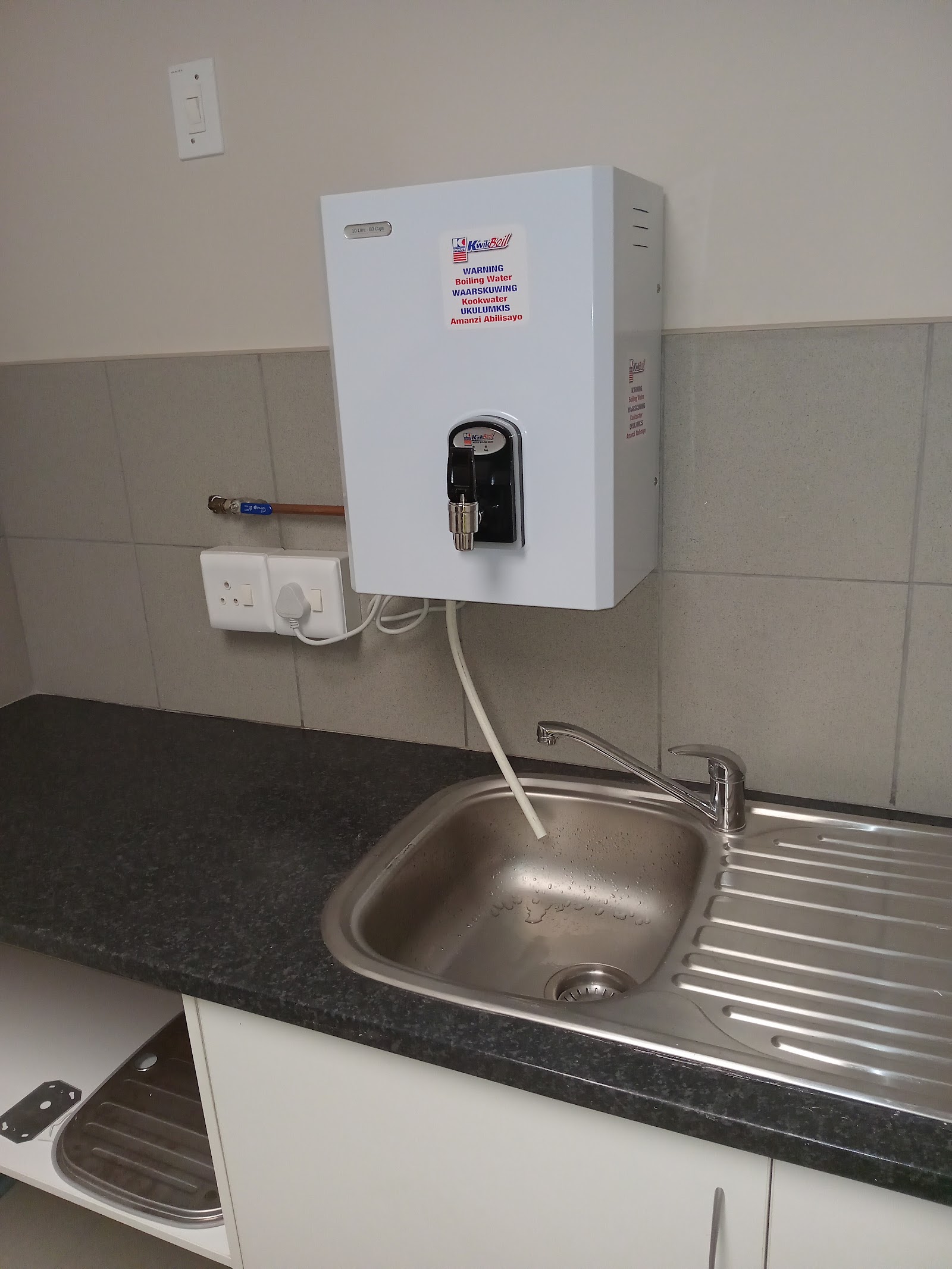 Kamooi brand instant water heater mounted above sink with warning labels visible.