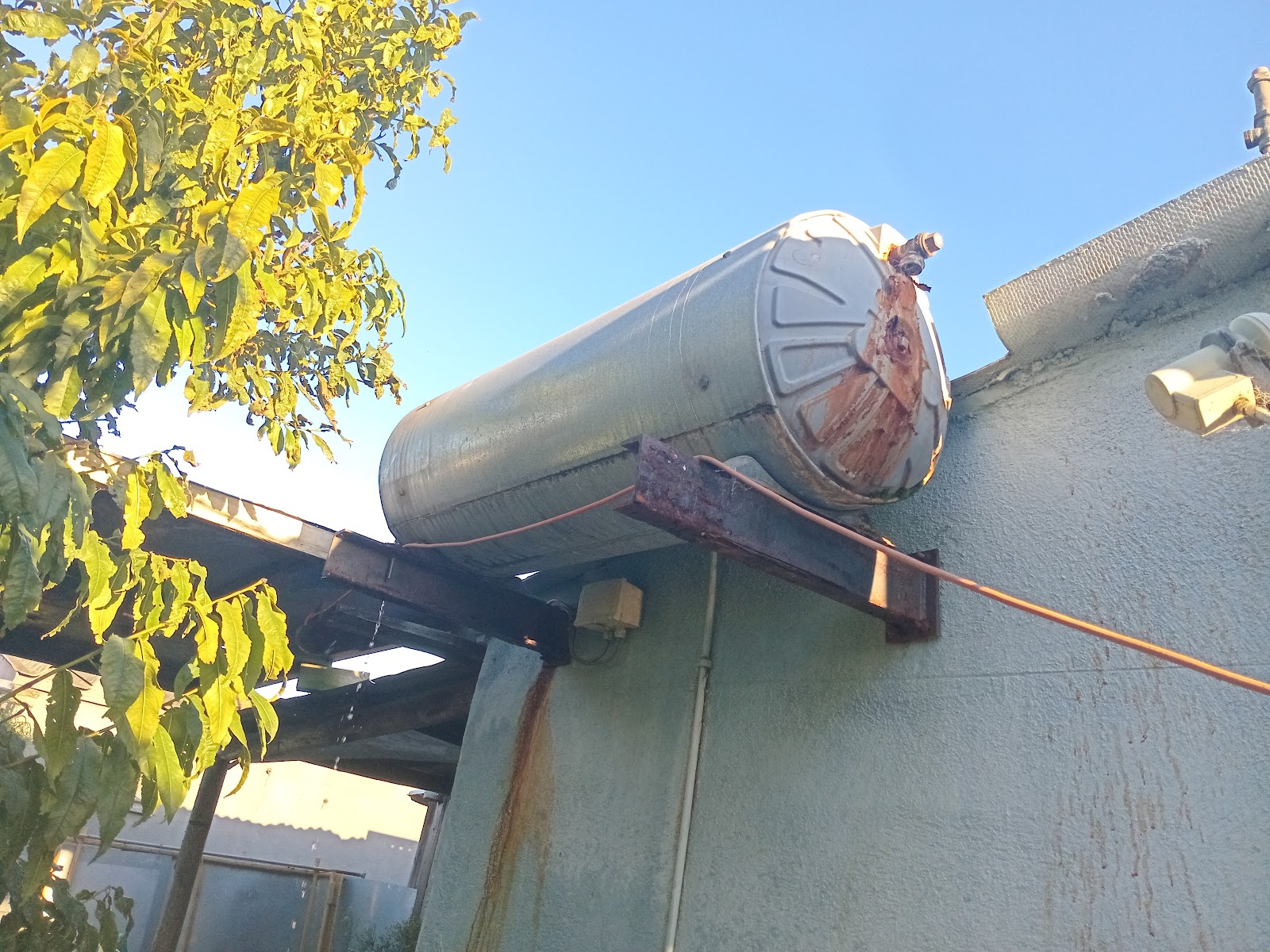 Corroded metal water storage tank mounted on building exterior with rust damage.