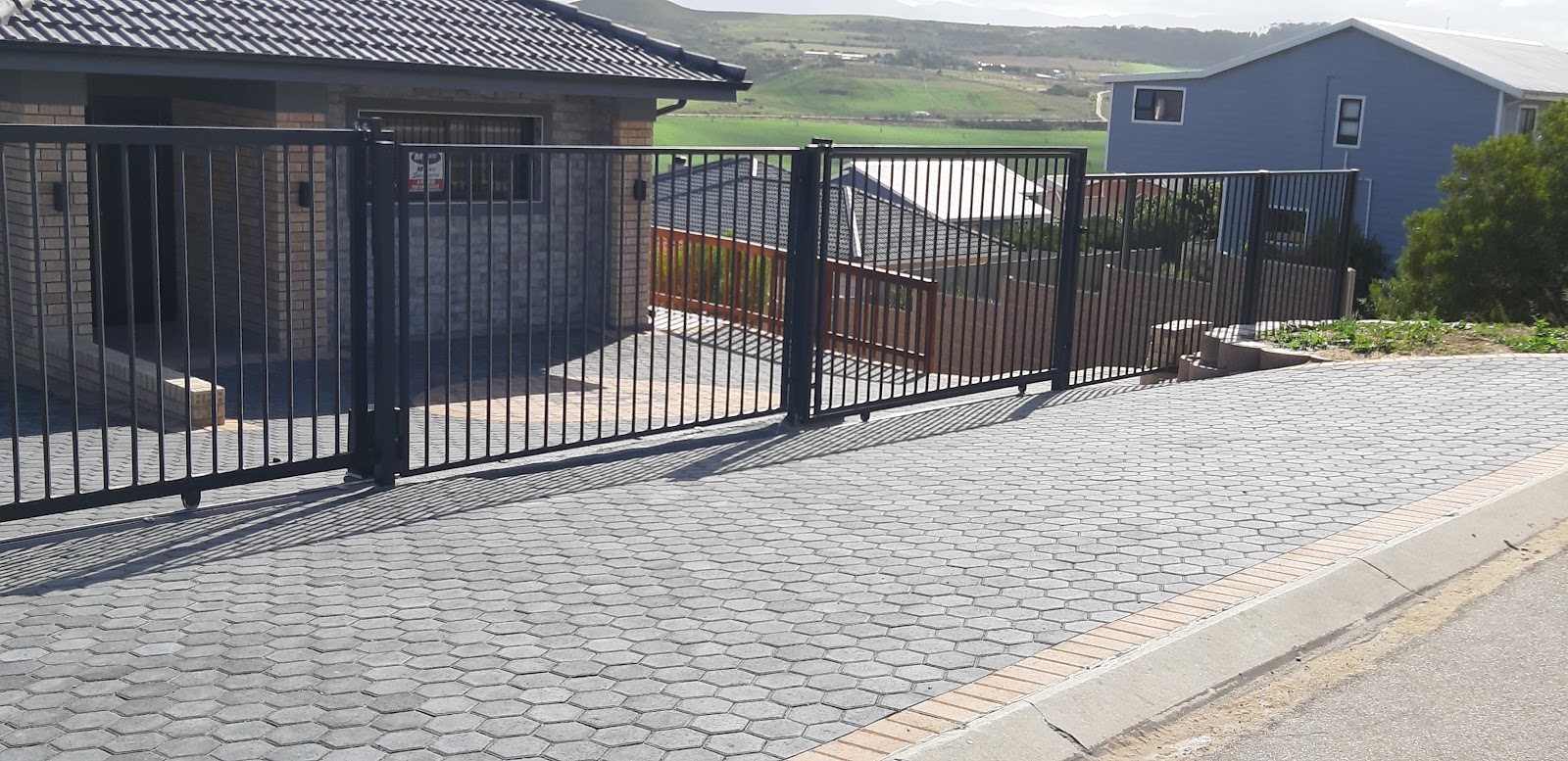 Black metal vertical bar gates with rust-colored wood accent panel on residential driveway.