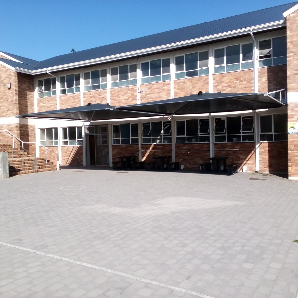 Black retractable awning installed over institutional brick building courtyard with windows and stairs.