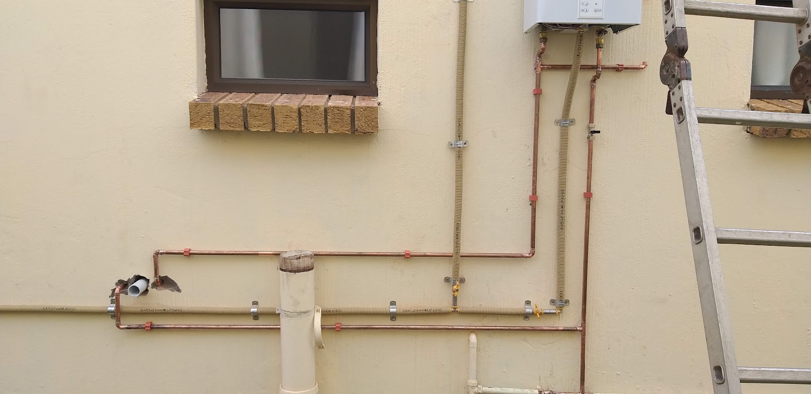 Interior plumbing installation showing multiple copper and PVC pipes with valves, ductwork above, monitor visible.