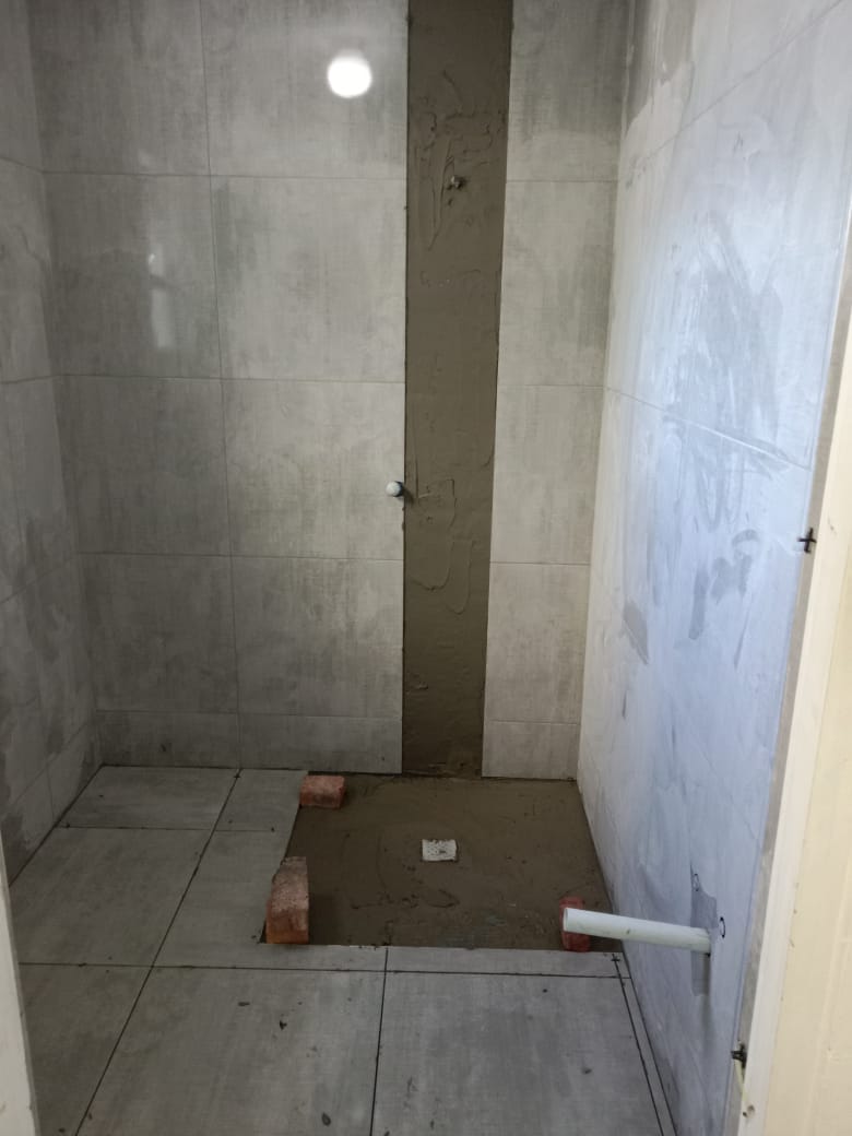 Unfinished shower enclosure with concrete floor, tiled walls, and central drain in progress.
