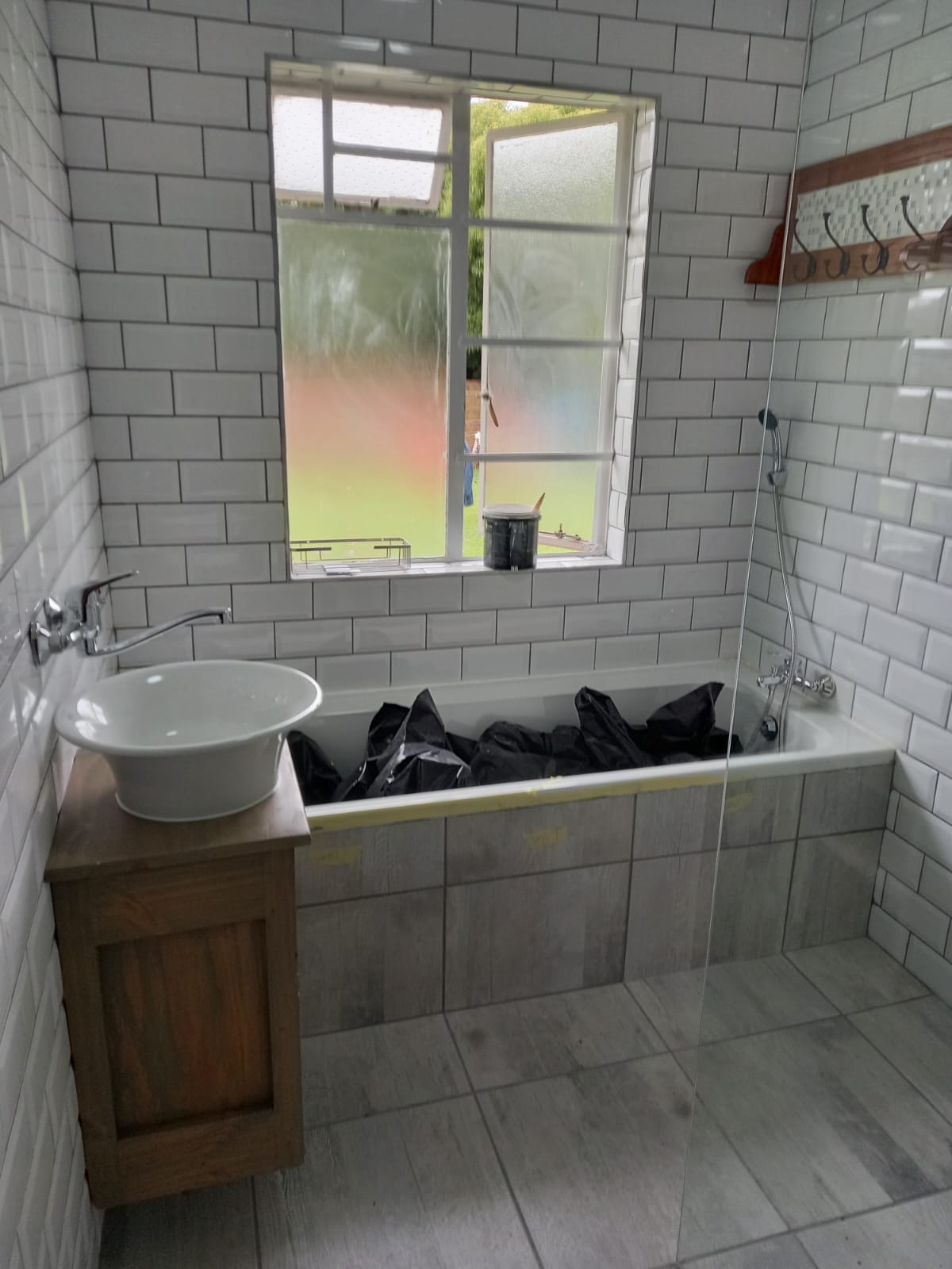 Completed bathroom with subway tile walls, installed window, pedestal sink, and bathtub with fixtures.