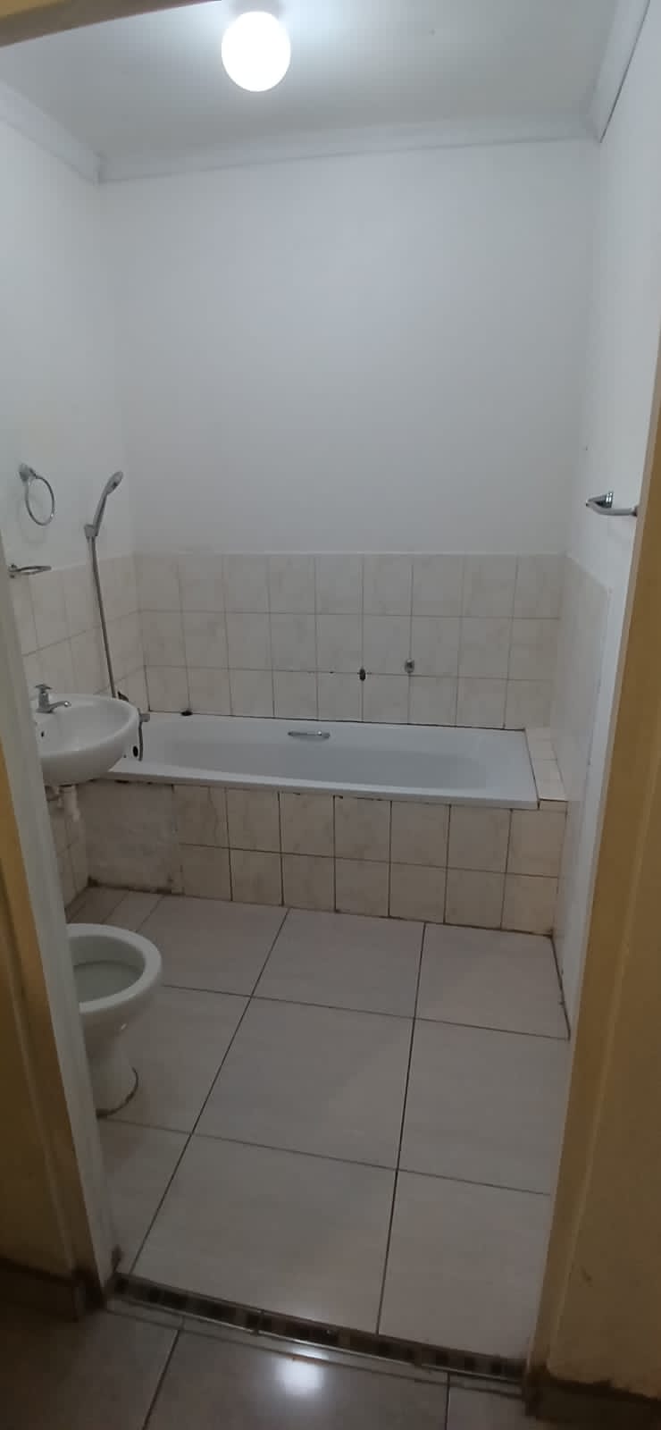 Finished compact bathroom with white tile, toilet, sink, and bathtub with shower enclosure.