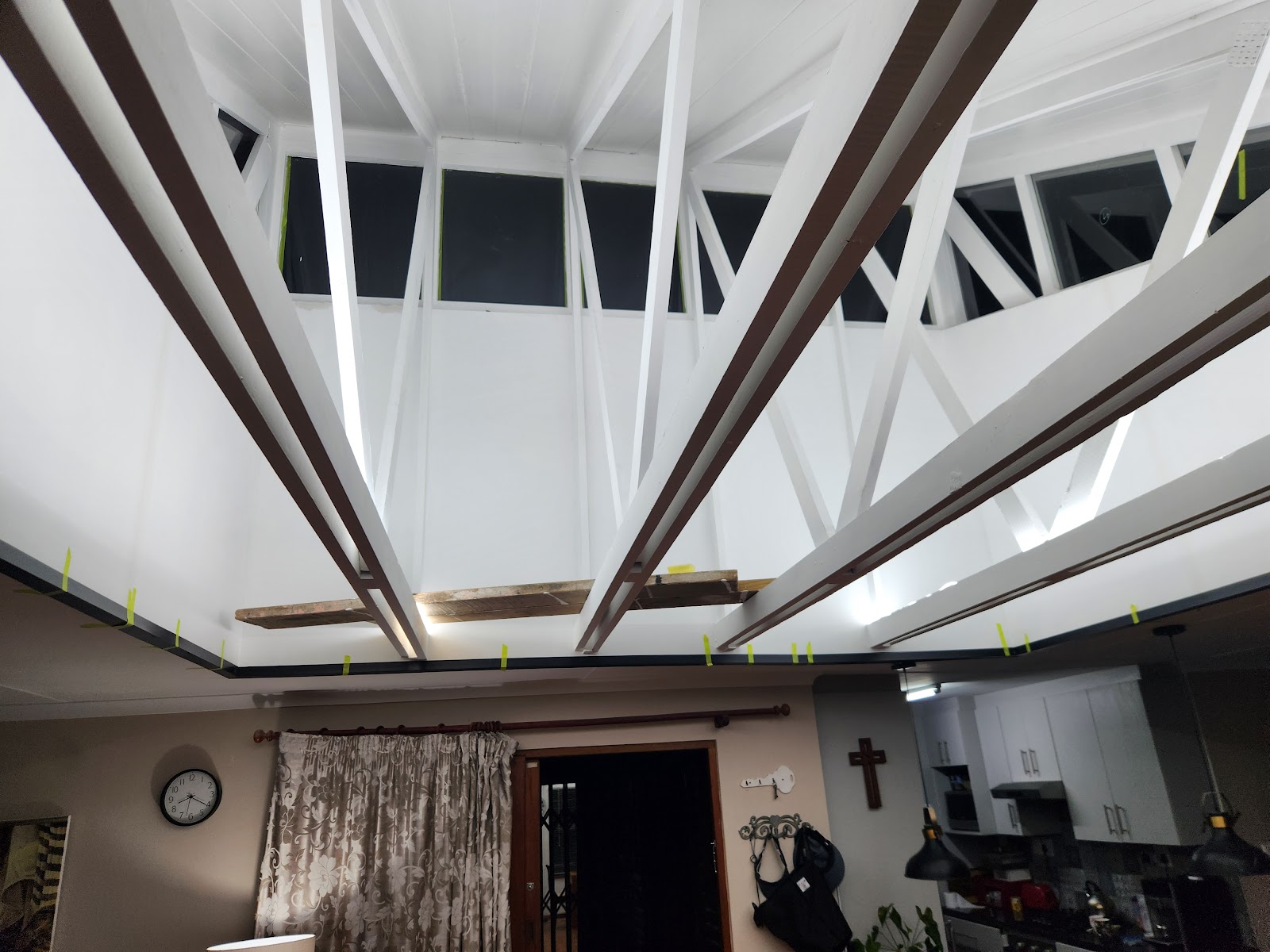Interior ceiling renovation showing white drywall, dark wooden beams, skylights, and yellow-marked installation points.