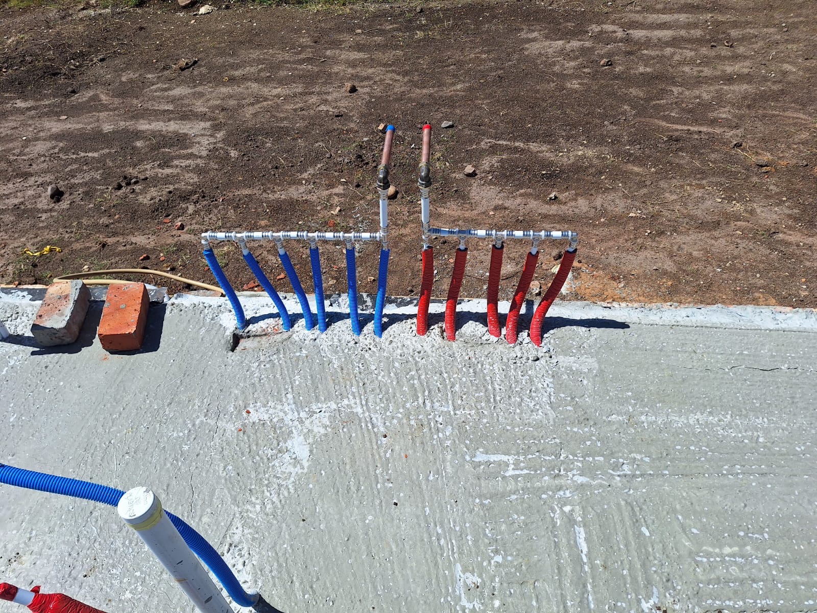Blue and red water supply lines laid in fresh concrete foundation with white PVC connectors visible.